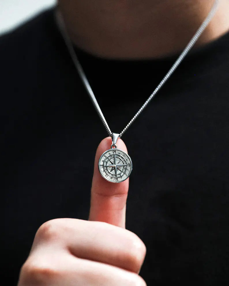 a man is holding a compass necklace in his hand