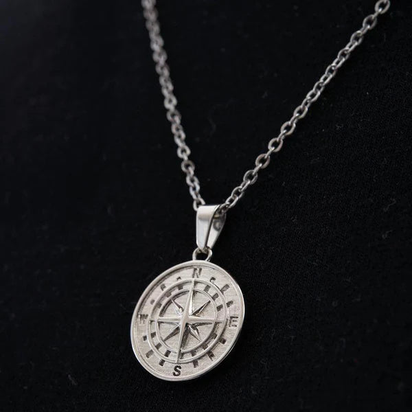 a silver compass necklace on a black background